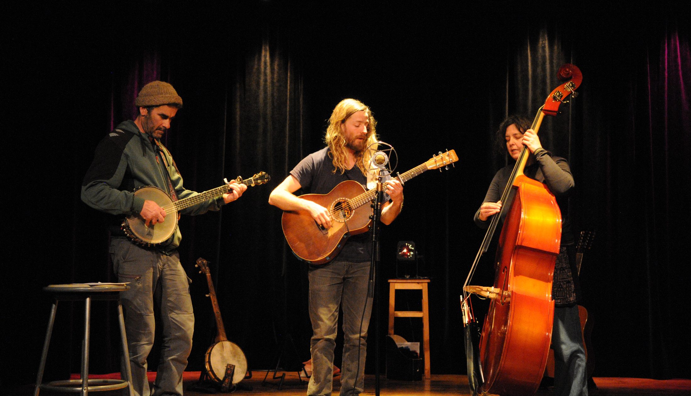 Les trois musiciens sur scène : banjo, guitare et contrebasse devant un rideau de velours noir.
