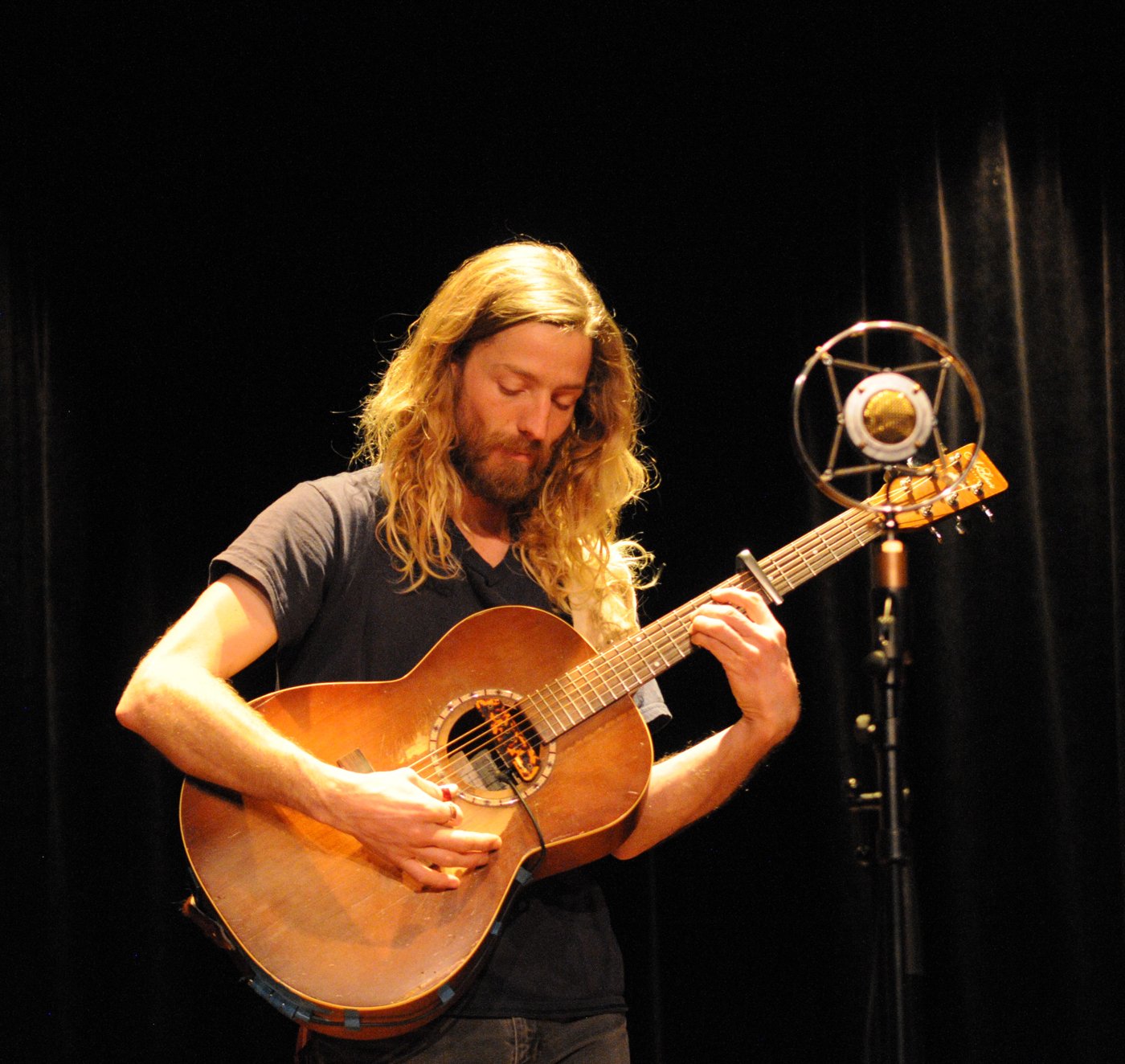 Le guitariste aux cheveux longs, tête penchée sur sa guitare, devant le micro.